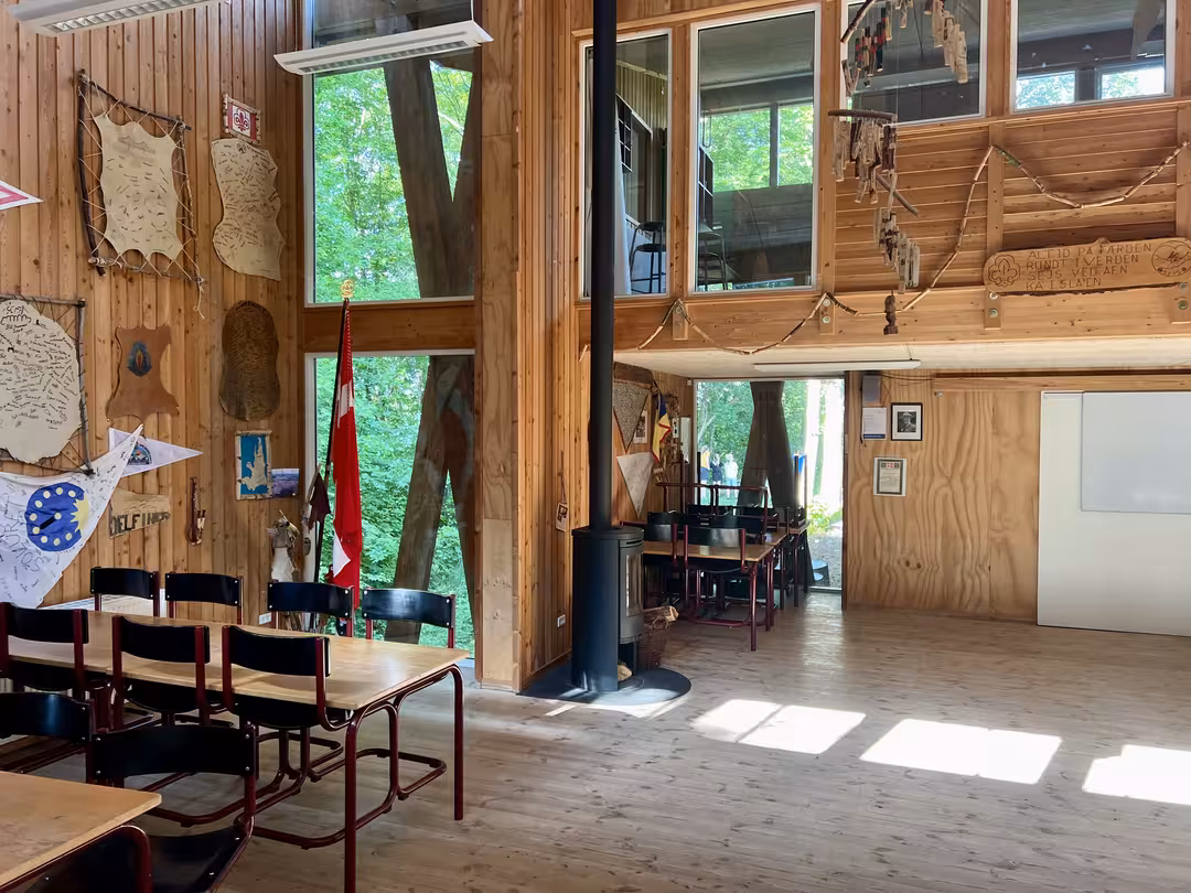 Fællesrum i Bjørnholthytten med dækkede borde og brændeovn